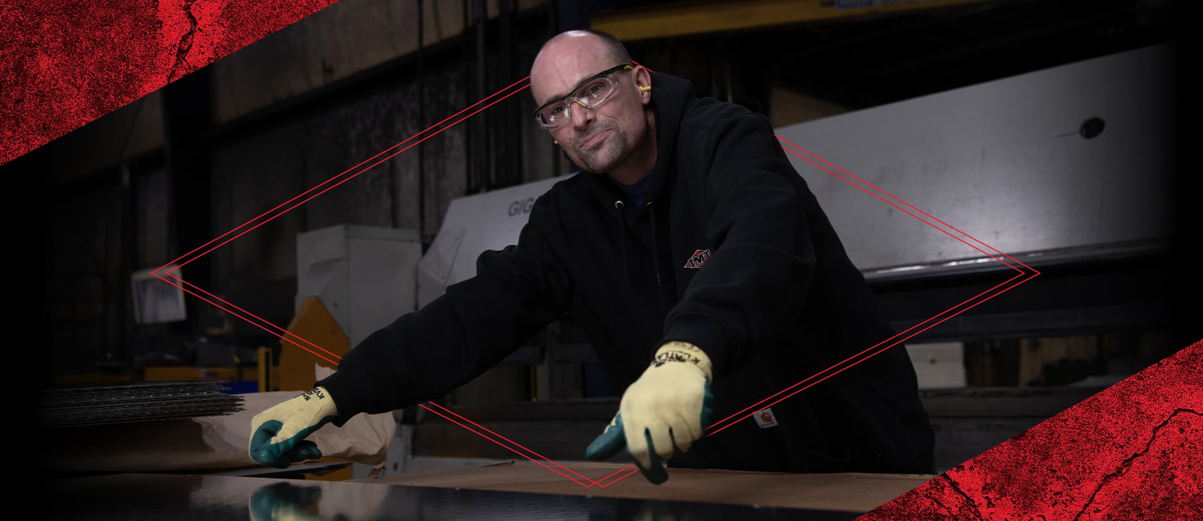 A Male Employee Working On A Sheet Of Metal Wearing A Black IMT Sweatshirt And Personal Protective Equipment.