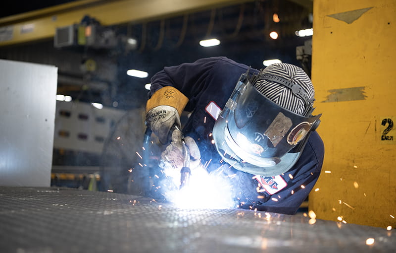 A Employee Welding A Sheet Of Metal Wearing Personal Protective Equipment.