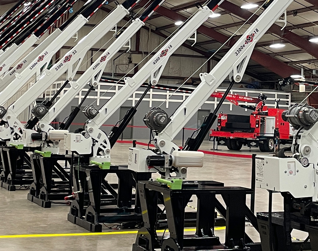 A fleet of new hydraulic service cranes lined up on display stands in a large showroom.
