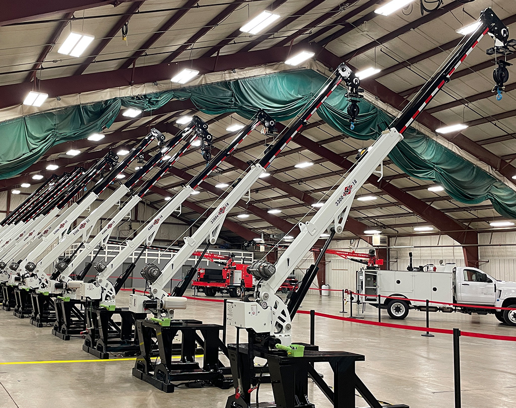 A long row of new service truck cranes on display inside a large warehouse.