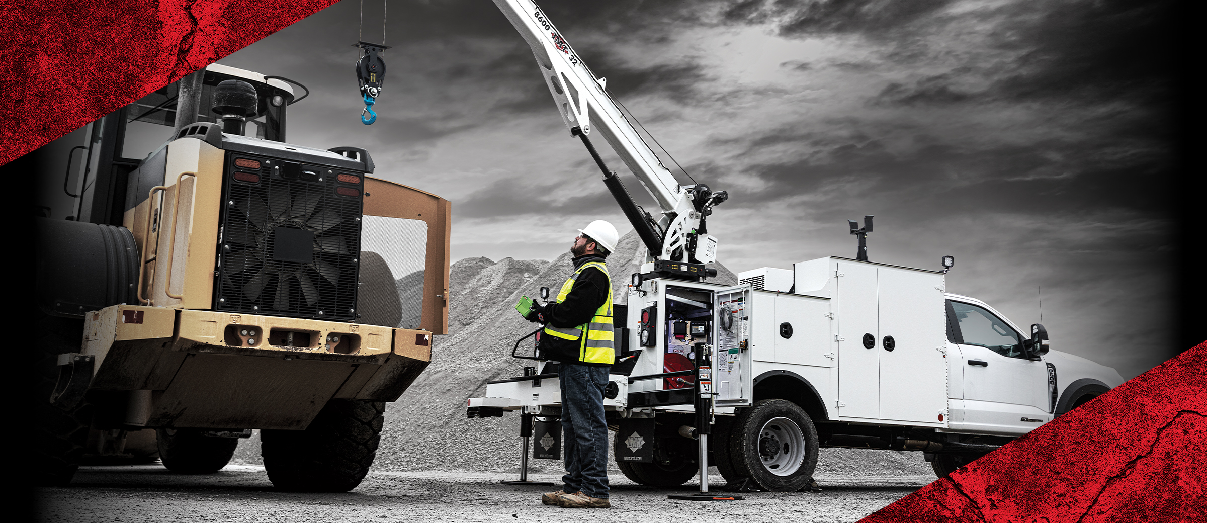 A technician in a safety vest operates a white service truck crane to perform maintenance on a large yellow tractor at a gravel site.
